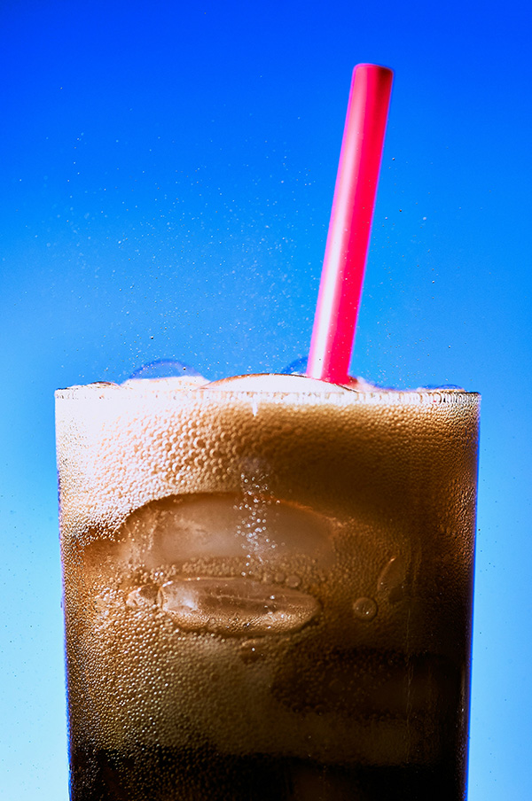 Close up of carbonated cola in a glass with pink plastic straw