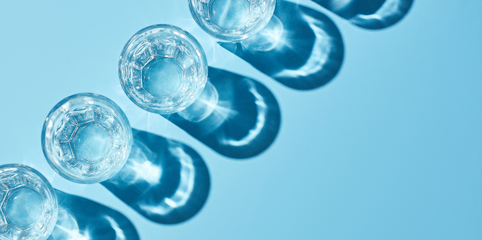 flat lay with glasses with clear water and shadows on blue background